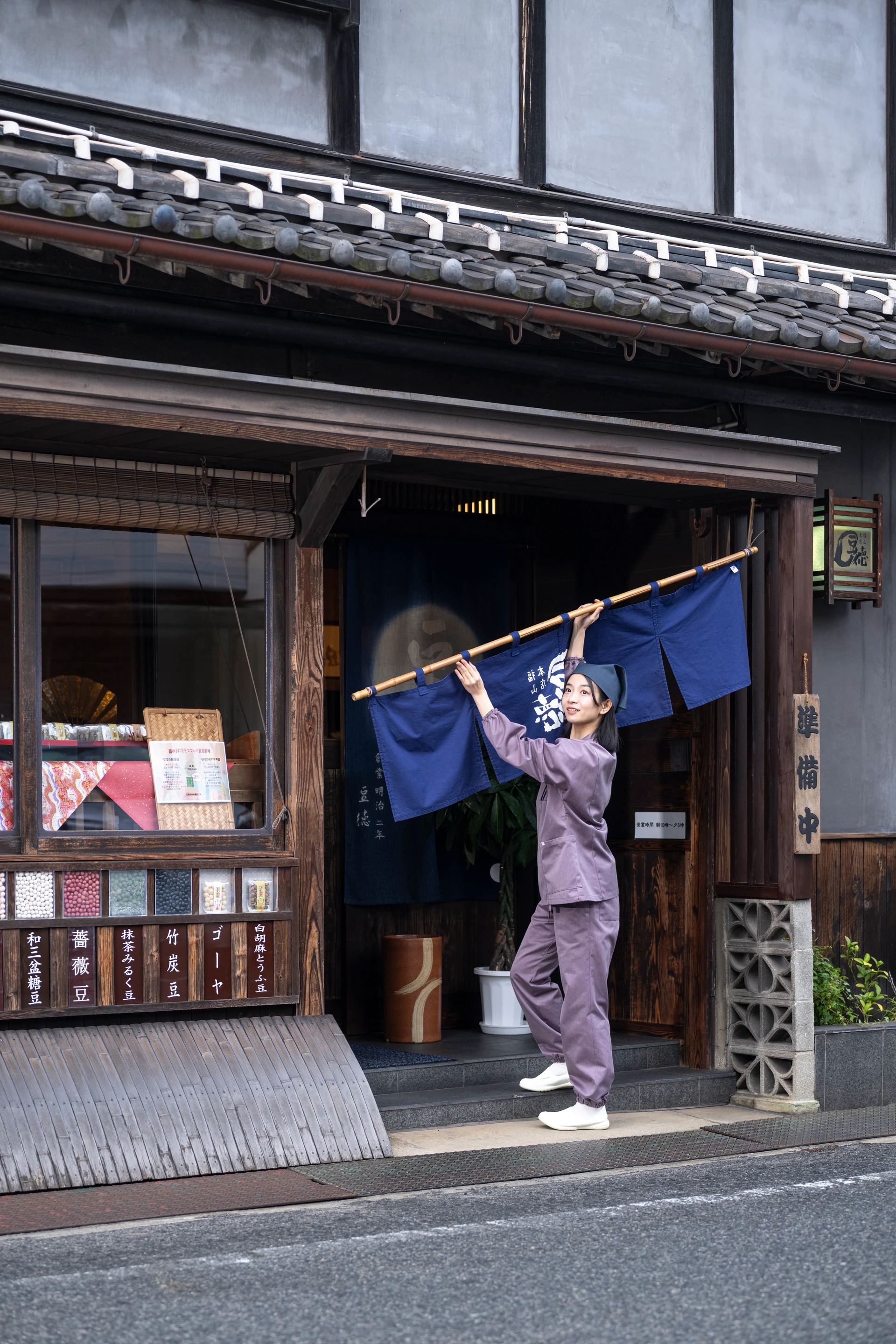 紫のユニフォームで暖簾を掛ける女性